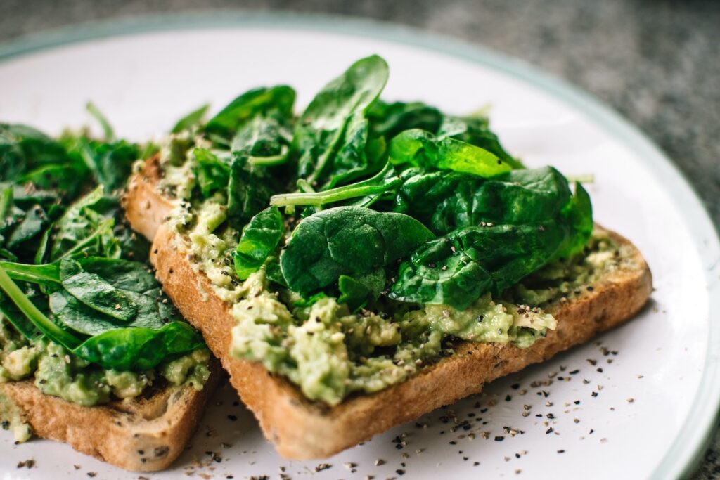 two slices of wheat toast topped with mashed avocado and topped with baby spinach leaves