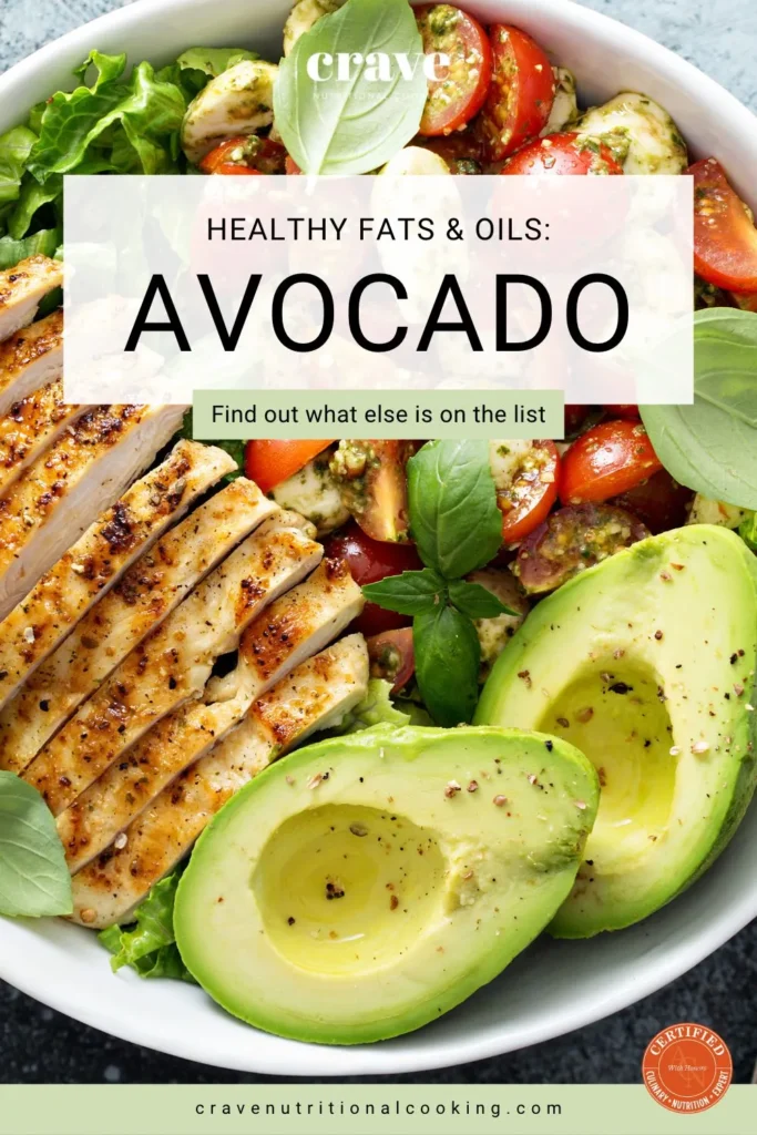 large round white bowl filled with slices of chicken breast and green salad ingredients with an avocado sliced open showing healthy fats